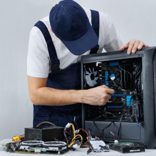 A computer engineer in uniform repairs a personal computer. A computer engineer in uniform repairs a personal computer